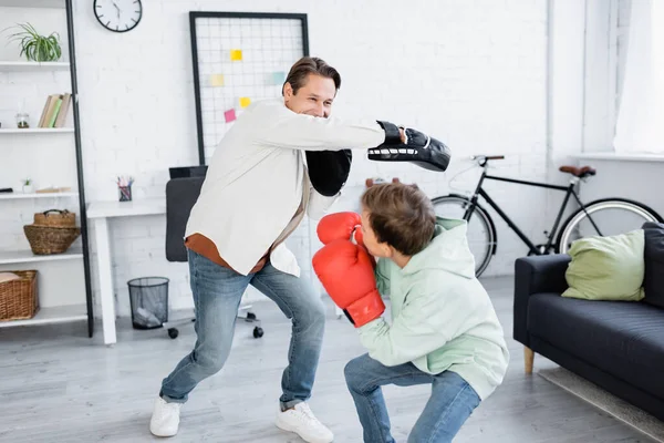 Papá y su hijo preadolescente en el entrenamiento de guantes de boxeo en la sala de estar - foto de stock