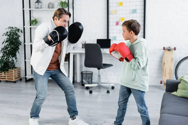 Mann mit Schlagpolstern schaut Sohn beim Boxen zu Hause an — Stockfoto