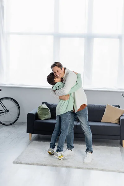 Preteen boy hugging smiling dad in living room — Stock Photo