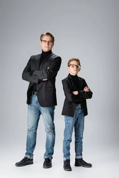 Padre e hijo en chaquetas cruzando brazos sobre fondo gris - foto de stock