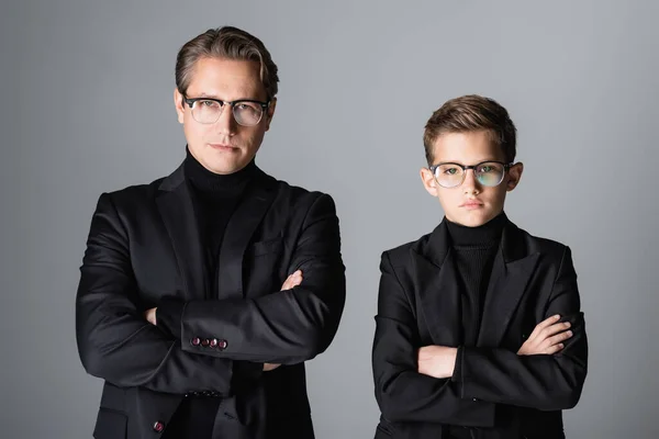 Stylish man and boy in jackets and eyeglasses crossing arms isolated on grey — Stock Photo