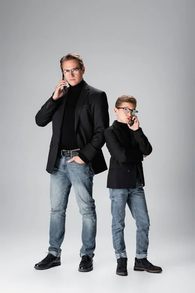 Full length of father and son talking on smartphones on grey background — Stock Photo