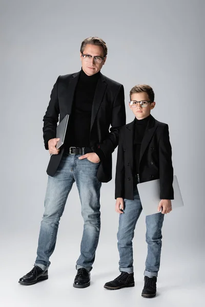 Stylish parent and son holding laptops on grey background — Stock Photo