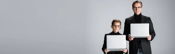 Preteen kid in jacket holding laptop near dad isolated on grey, banner — Stockfoto