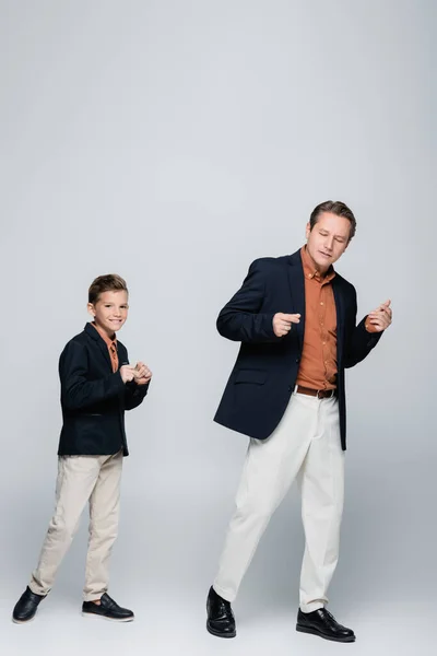 Hombre y elegante hijo preadolescente bailando sobre fondo gris - foto de stock