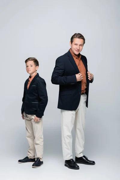 Full length of stylish boy and father looking at camera on grey background — Stock Photo