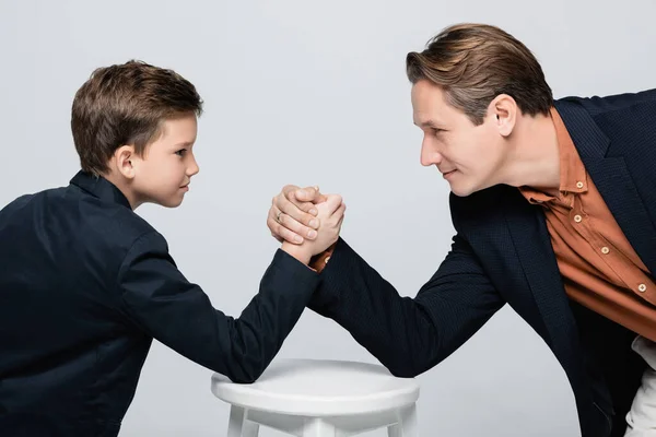 Seitenansicht von Vater und Sohn, die sich beim Armdrücken isoliert auf grau anschauen — Stockfoto
