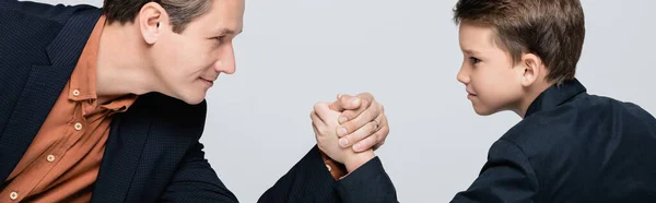 Vista laterale del padre in giacca che tiene la mano del figlio durante il braccio di ferro isolato su grigio, banner — Foto stock