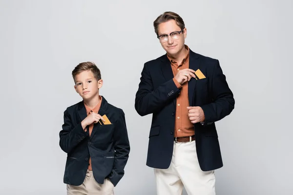Stylish father and son taking credit cards from pockets of jackets isolated on grey — Stock Photo