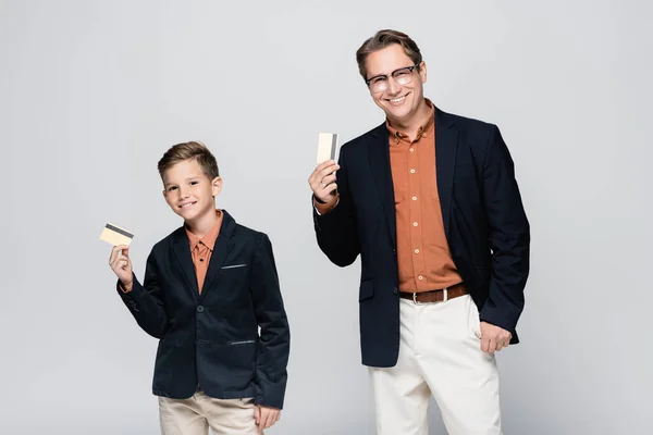 Smiling dad and son holding credit cards isolated on grey — Stock Photo