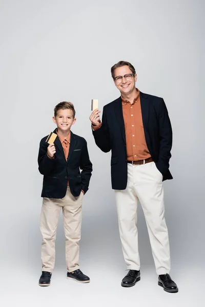 Longitud completa de elegante niño y padre con tarjetas de crédito sobre fondo gris - foto de stock