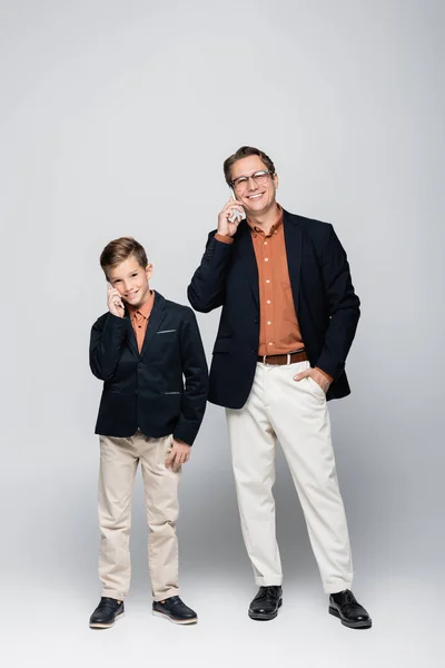 Alegre padre e hijo con estilo hablando en teléfonos inteligentes sobre fondo gris - foto de stock