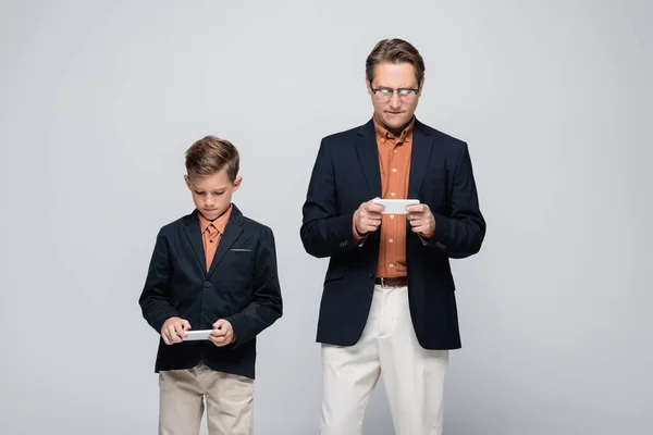 Padre e hijo en chaquetas usando teléfonos celulares aislados en gris - foto de stock