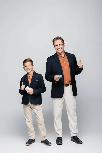 Lächelnder Vater und Sohn mit Smartphones auf grauem Hintergrund — Stockfoto