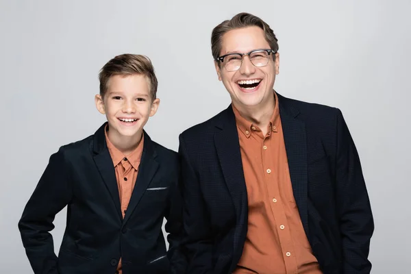Счастливые стильные отец и сын смотрят в камеру, изолированную от серого — стоковое фото