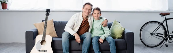 Cheerful father hugging son near acoustic guitar at home, banner — Stock Photo