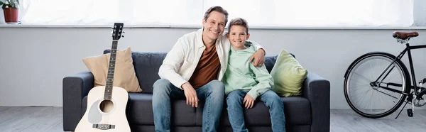 Alegre padre abrazando hijo cerca de la guitarra acústica en casa, bandera - foto de stock