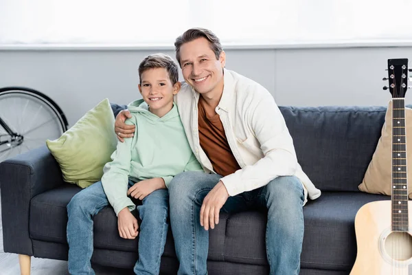 Father hugging preteen boy near acoustic guitar in living room — Stock Photo