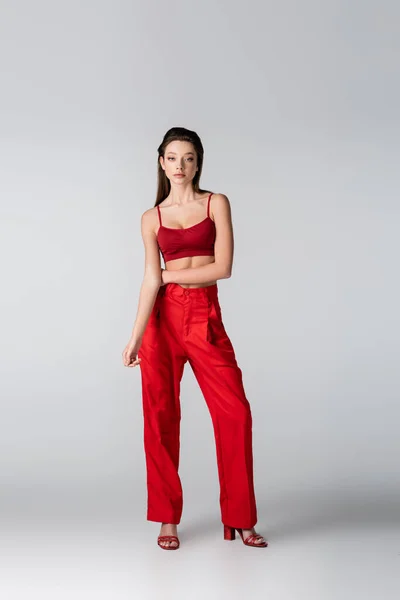 Longitud completa de la joven modelo bonita en traje rojo posando en gris - foto de stock