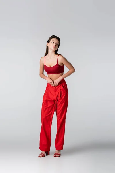 Piena lunghezza di grazioso modello in abito rosso guardando altrove sul grigio — Foto stock