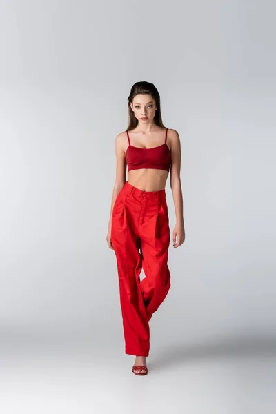 Longitud completa de modelo joven en traje rojo elegante posando en gris - foto de stock