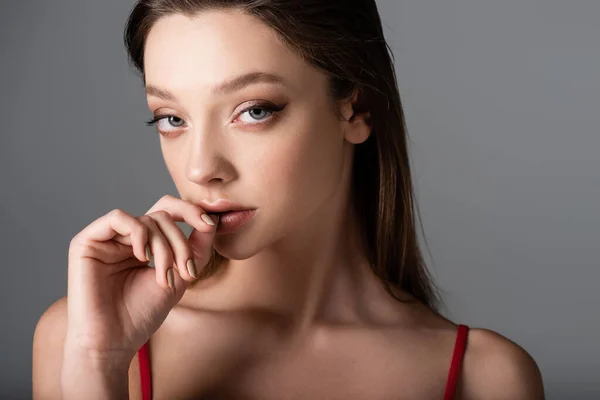 Primer plano de mujer joven con maquillaje tocando los labios y mirando a la cámara aislada en gris oscuro - foto de stock