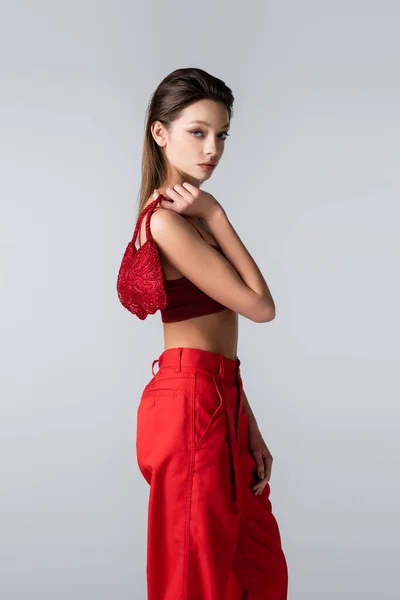 Junge Frau im roten Outfit mit stylischer Tasche isoliert auf grau — Stockfoto