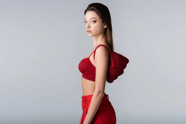 Bonita mujer en traje rojo con elegante bolso en el hombro aislado en gris - foto de stock