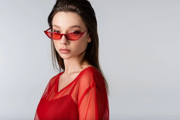 Молода модель в червоних модних сонцезахисних окулярах ізольована на сірому — стокове фото