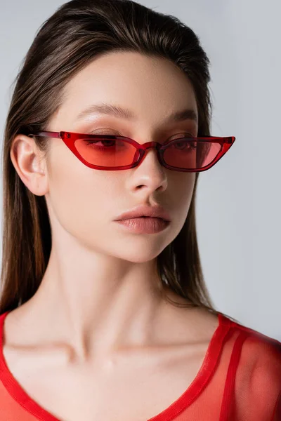 Modelo joven en gafas de sol rojas de moda aisladas en gris - foto de stock