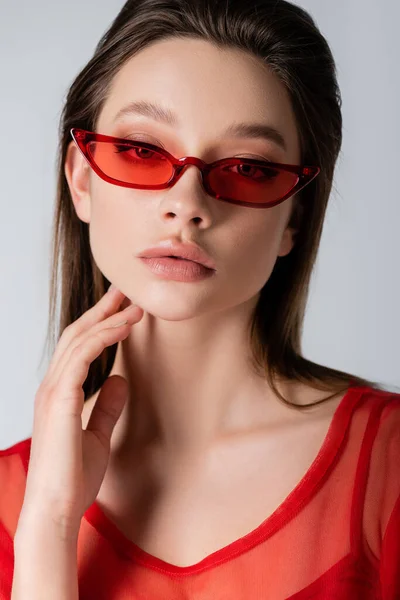 Modelo joven en gafas de sol elegantes rojas aisladas en gris - foto de stock