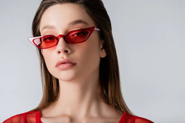 Young model in red trendy sunglasses looking at camera isolated on grey — Stock Photo