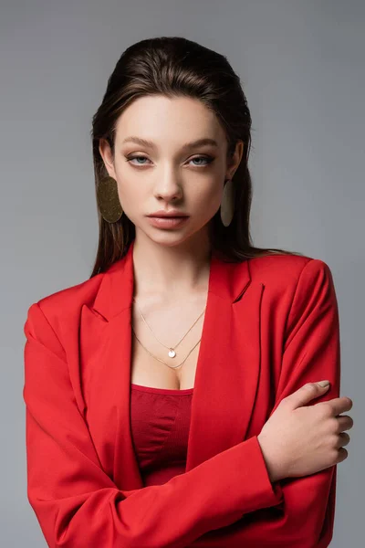 Pretty woman in red blazer and earrings looking at camera isolated on grey — Stock Photo