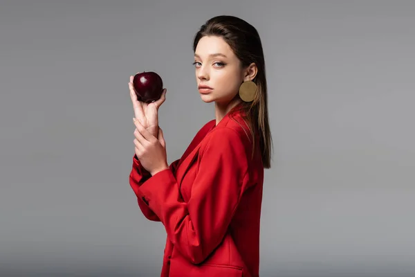 Junge hübsche Frau im roten Anzug hält Apfel isoliert auf grau — Stockfoto