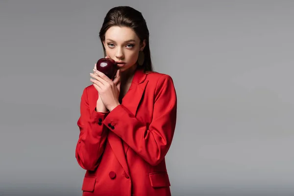 Jeune femme en blazer rouge tenant pomme isolée sur gris — Photo de stock