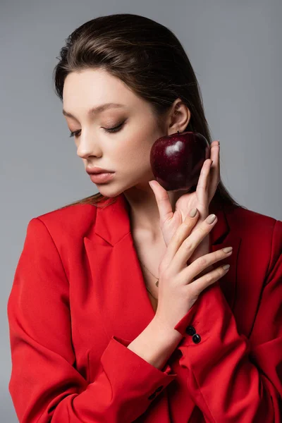 Молодая модель в красном блейзере, держащая яблоко изолировано на сером — стоковое фото