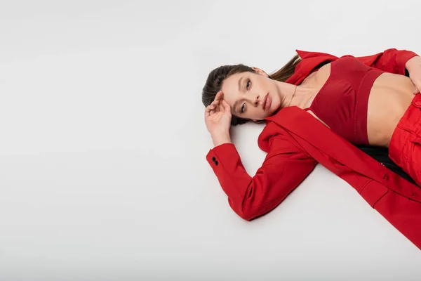 Vista de ángulo alto de la mujer joven de moda en traje rojo acostado aislado en gris - foto de stock