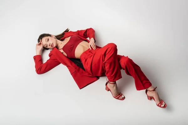 Высокий угол обзора стильной молодой женщины в красном наряде, лежащей на сером — стоковое фото