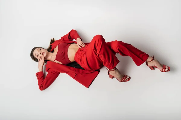 Высокий угол обзора стильной молодой женщины в красной одежде и обуви, лежащих на сером — стоковое фото