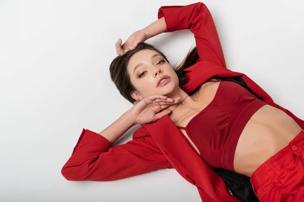 Draufsicht auf trendige junge Frau im roten Anzug, die auf grau liegt — Stockfoto