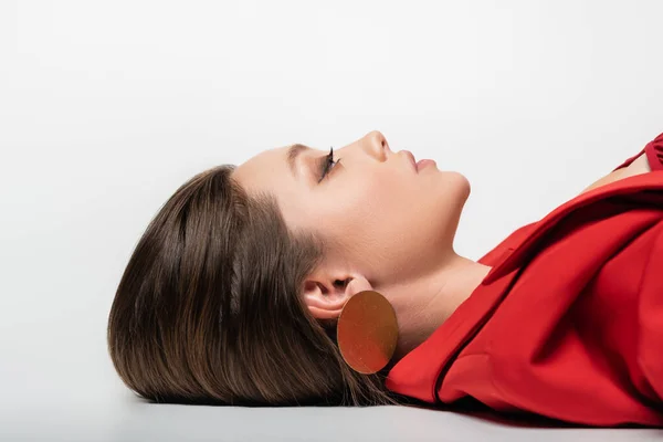 Вид сбоку на триумфальную молодую женщину в красном блейзере, лежащую на сером — стоковое фото