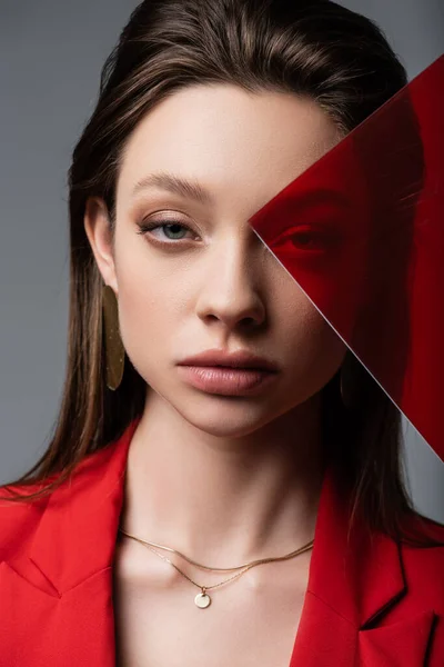 Молода модель дивиться на камеру через червоне скло ізольовано на сірому — стокове фото
