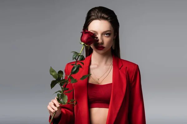 Молода жінка в червоному вбранні тримає троянду ізольовано на сірому — стокове фото
