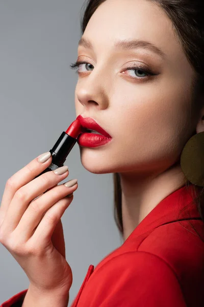 Primer plano del modelo joven aplicando lápiz labial rojo aislado en gris - foto de stock