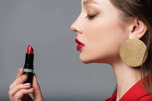 Side view of young model holding red lipstick isolated on grey — Stock Photo