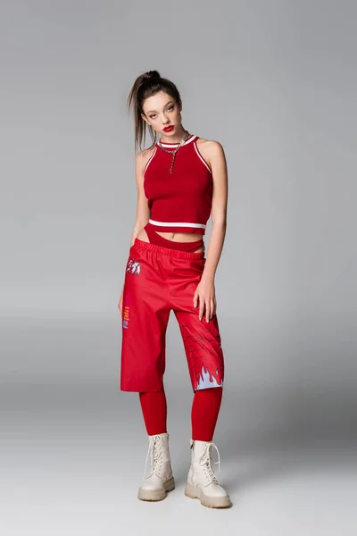 Pleine longueur de jeune femme en tenue de sport rouge posant sur gris — Photo de stock