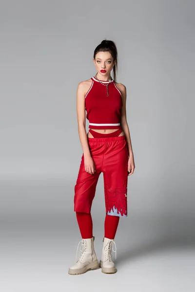 Longueur totale du jeune modèle en tenue de sport rouge et bottes debout sur gris — Photo de stock