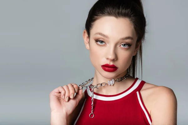 Young stylish woman with red lips pulling necklace chain isolated on grey — Stock Photo