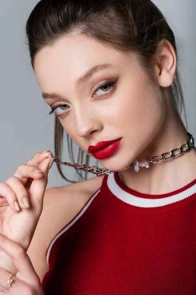 Modelo joven con labios rojos tirando cadena collar aislado en gris - foto de stock