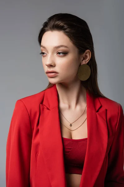 Mujer joven con estilo en chaqueta roja mirando hacia otro lado aislado en gris - foto de stock